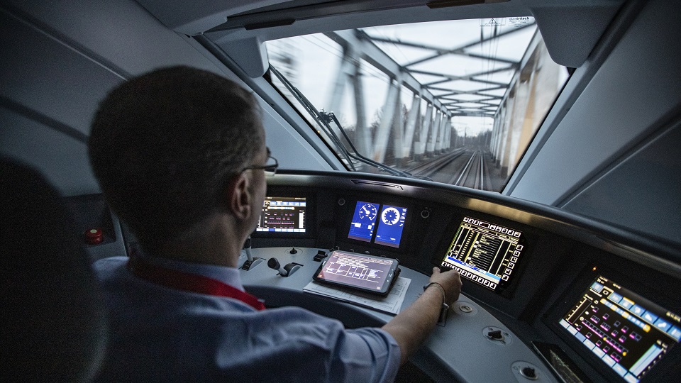 A train driver inside a train cab looking out at the track in front of him