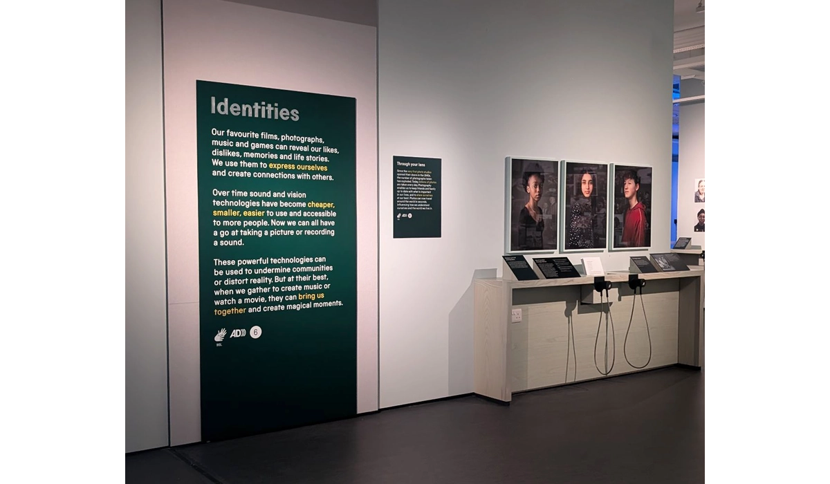 A section of the Sound + Vision galleries on Identities. A green board with white writing explains how people express themselves through their favourite films and music. Three photographic portraits of young people are on the wall nearby, with further information and resources to listen to transcripts.