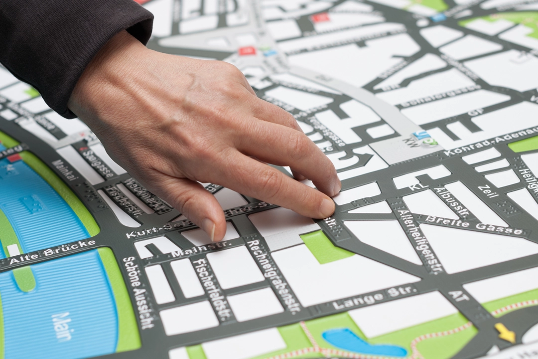 A hand hovering over and touching a tactile map showing street names in braille and different textures to identify different areas.