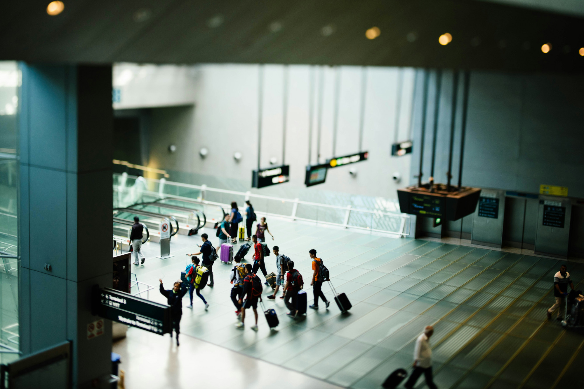 People walking onto an escalator in a wide open airport terminal or station
