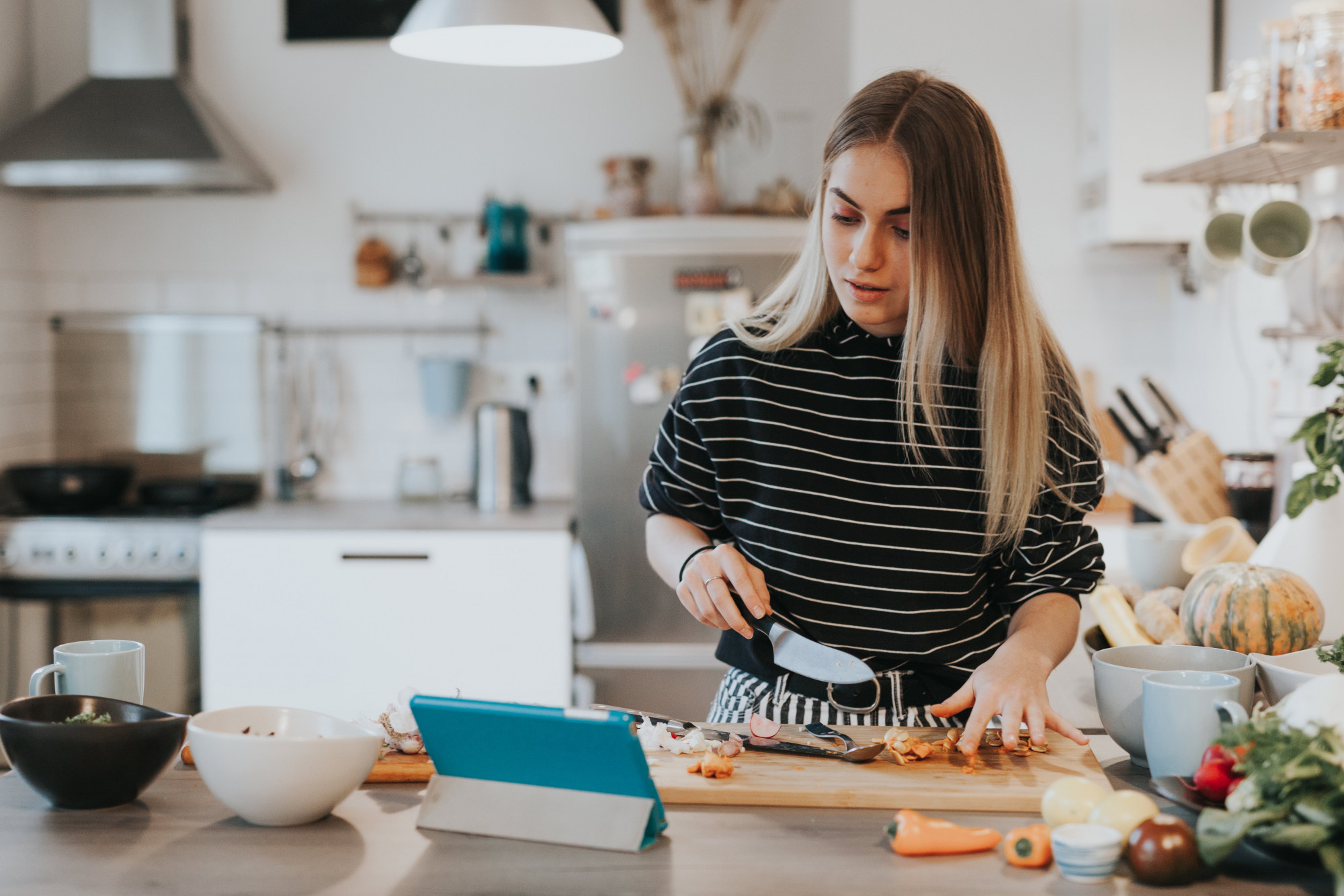 A woman chops carrots whilst checking a tablet for instructions