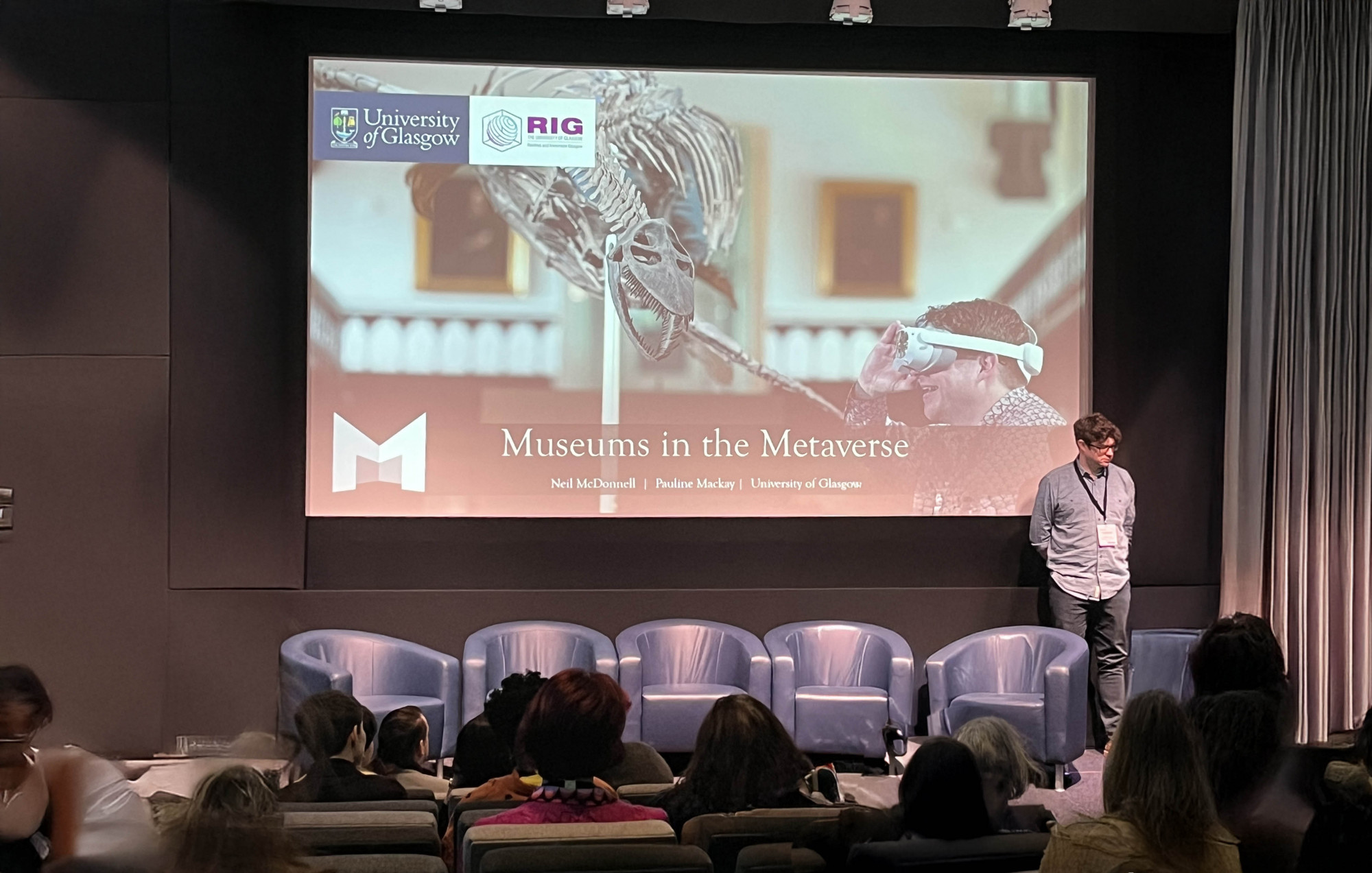 Presentation with visitors seated in front of a screen with a title Museums in the Metaverse