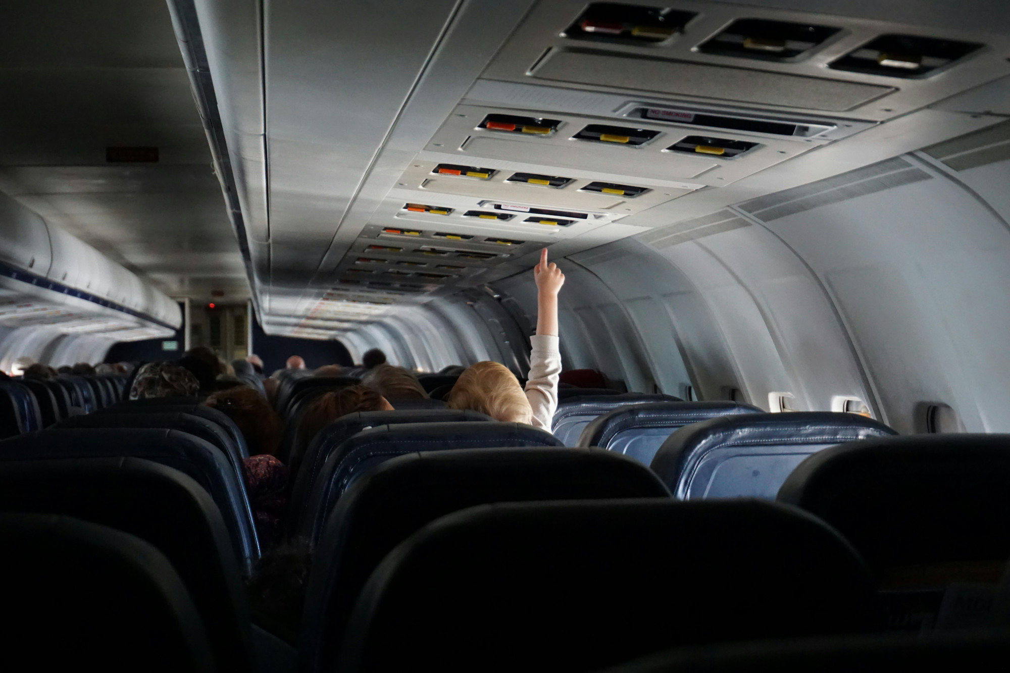 A child reaches up to press the buttons above the seat in a plane