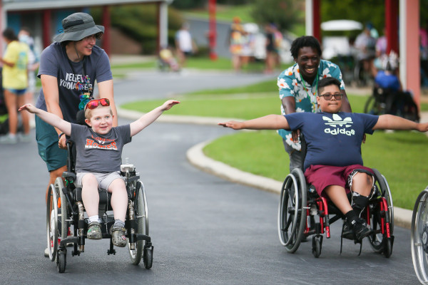 A picture of a two smiling children in wheelchairs being pushed by members of the Serious Fun team